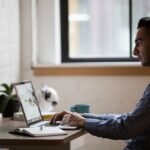 Man sitting at desk working on laptop with a cup of coffee