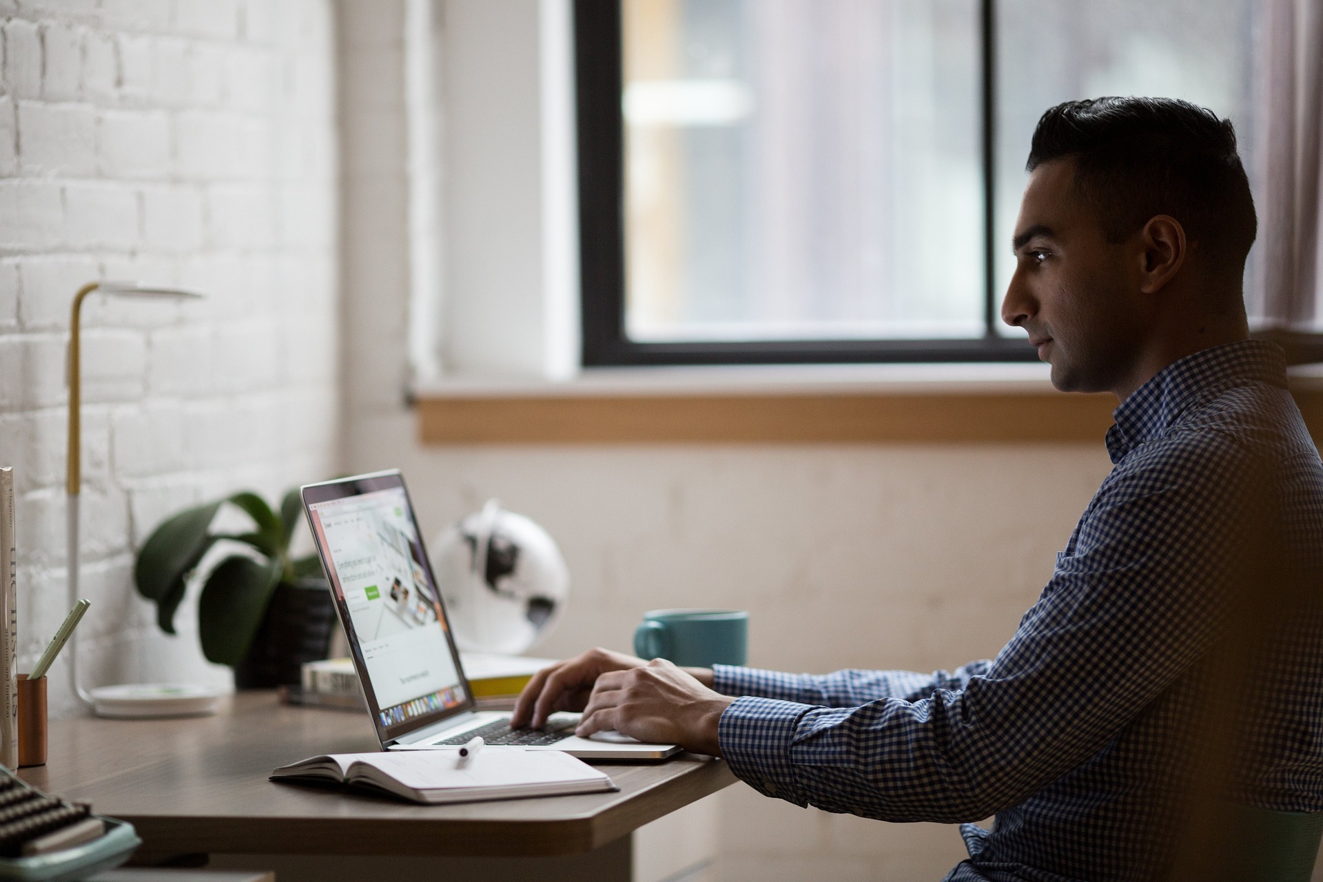 Man sitting at desk working on laptop with a cup of coffee